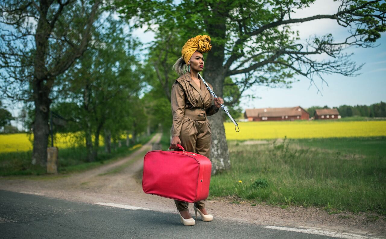 A woman stands at a crossroads with a red bag.