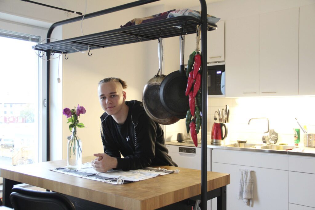 A guy standing in his kitchen and hanging over a kitchen counter.