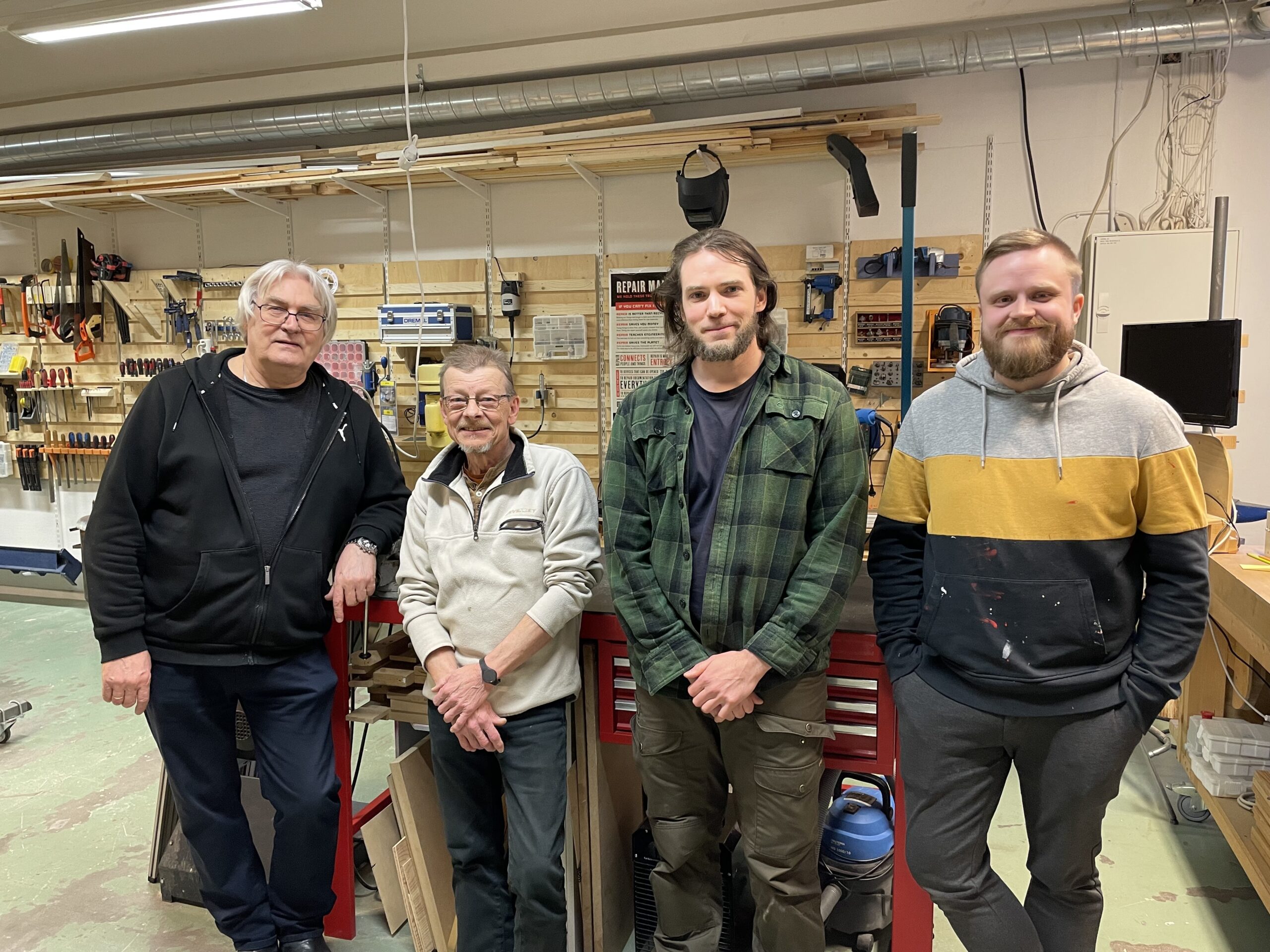 Four men standing in front of a tool bench in a workshop