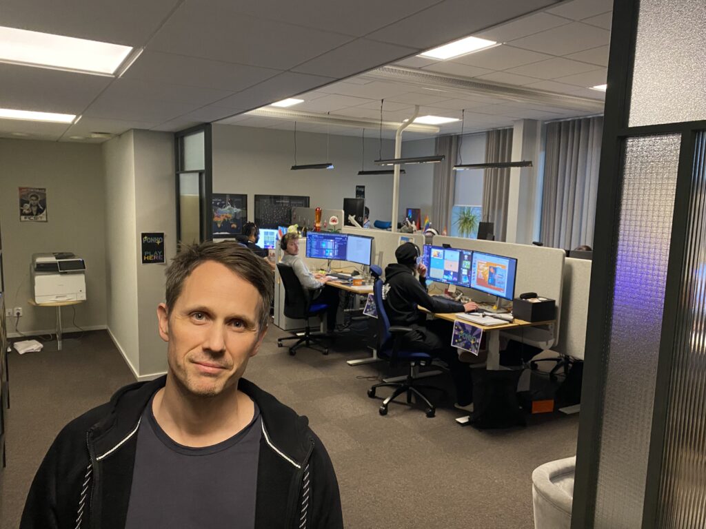 En leende man i förgrunden och människor vid datorer i bakgrunden.