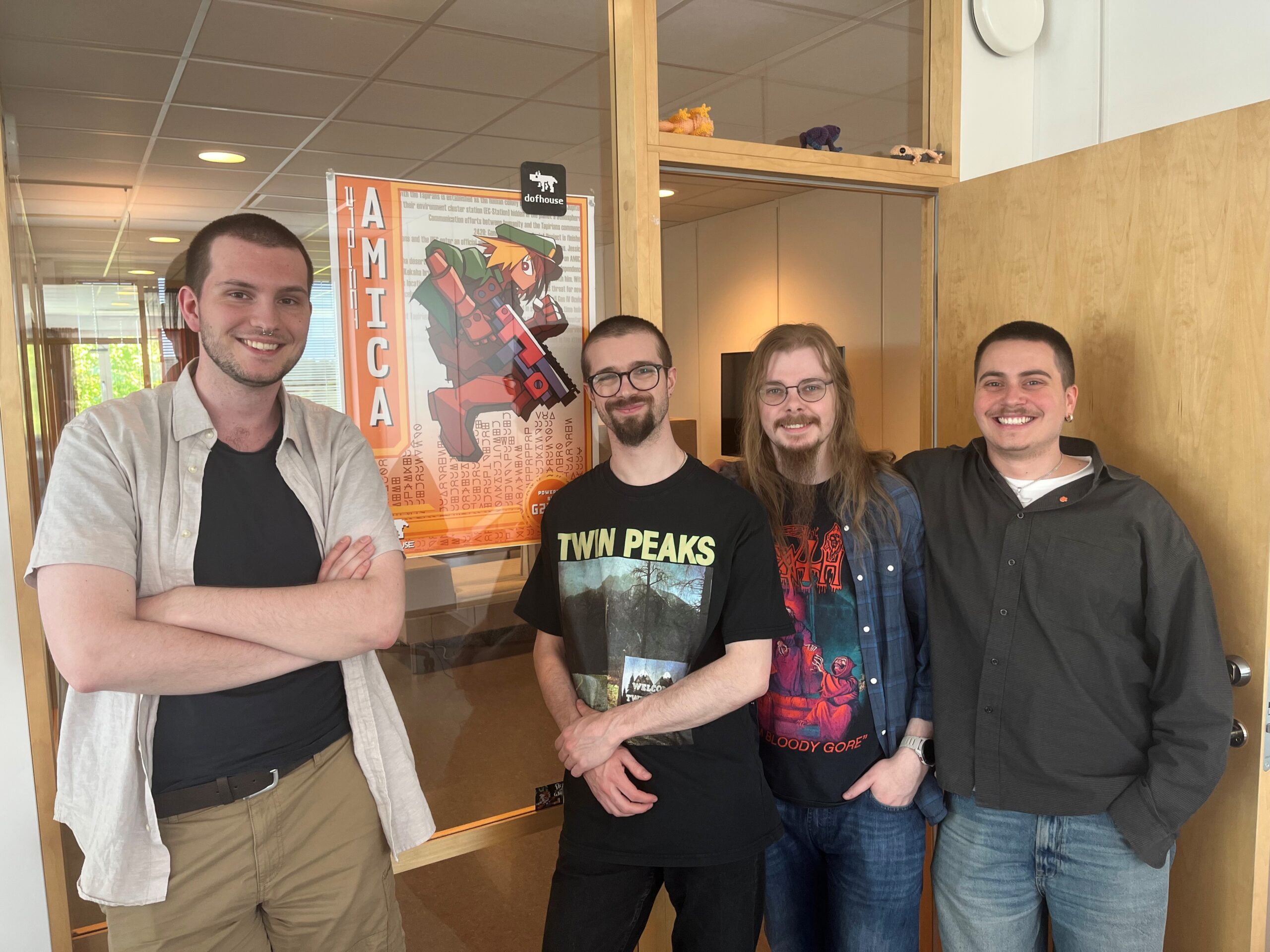 Four guys are leaning against a wall with a Project Amica poster in the background