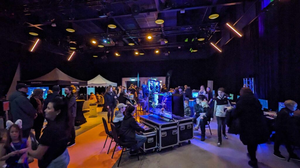 Ett spelevent med personer i olika åldrar som sitter och spelar olika dataspel i ett mörkt rum.