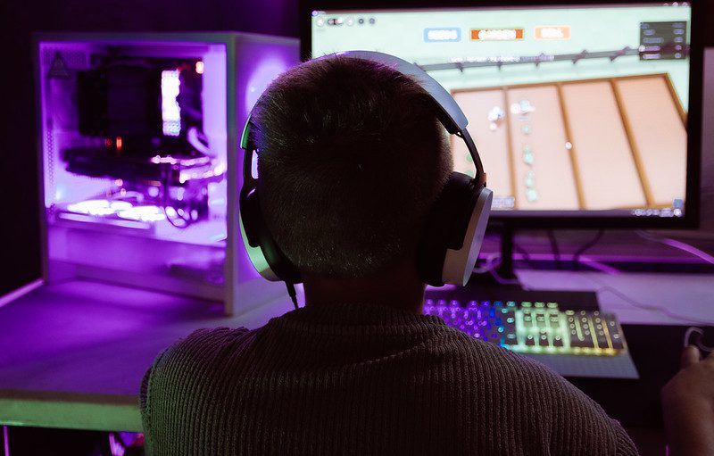 En person sitter och tittar på en spelskärm. Den har på sig hörlurar.