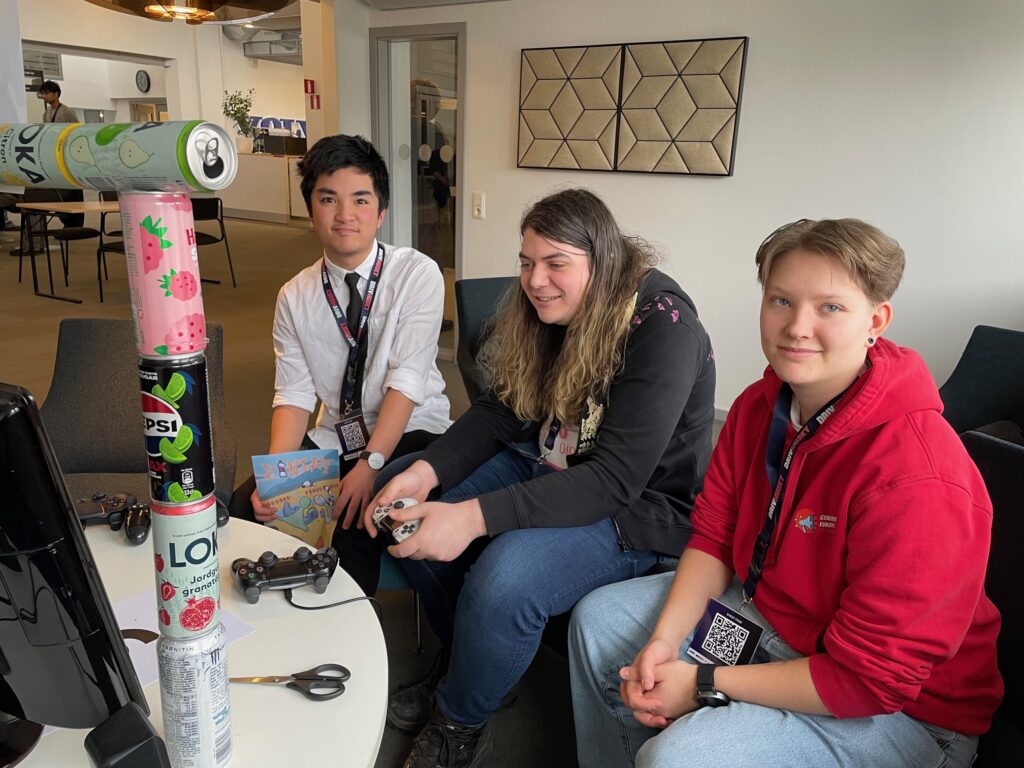 Tre unga människor sitter vid ett bord och arbetar med ett dataspel