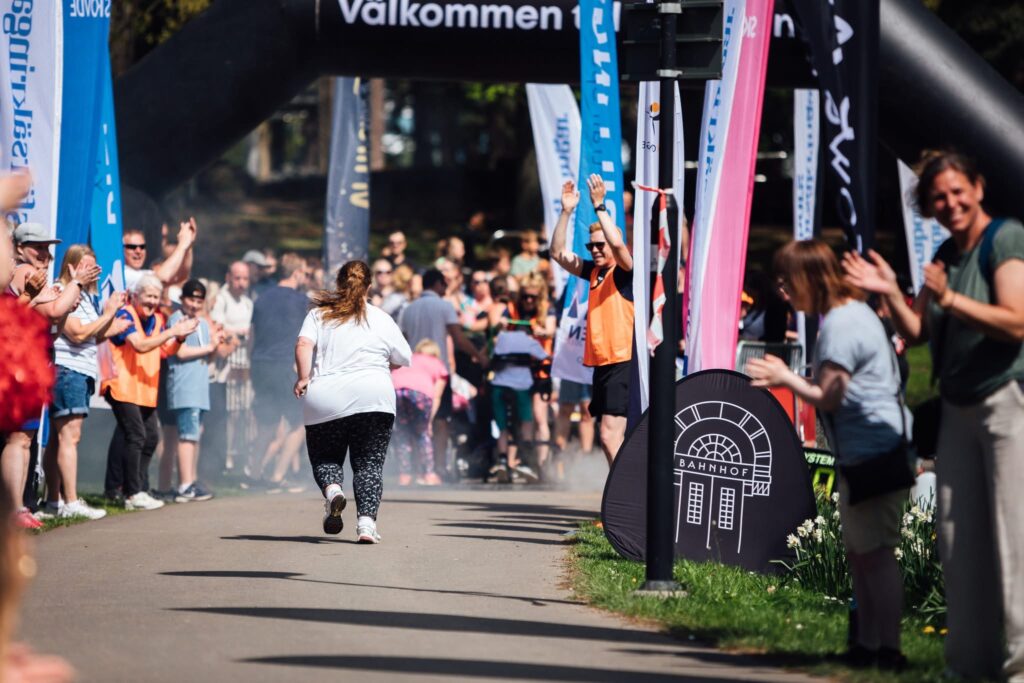 Girl running a race on an asphalt road. on both sides there is a crowed cheering her on.