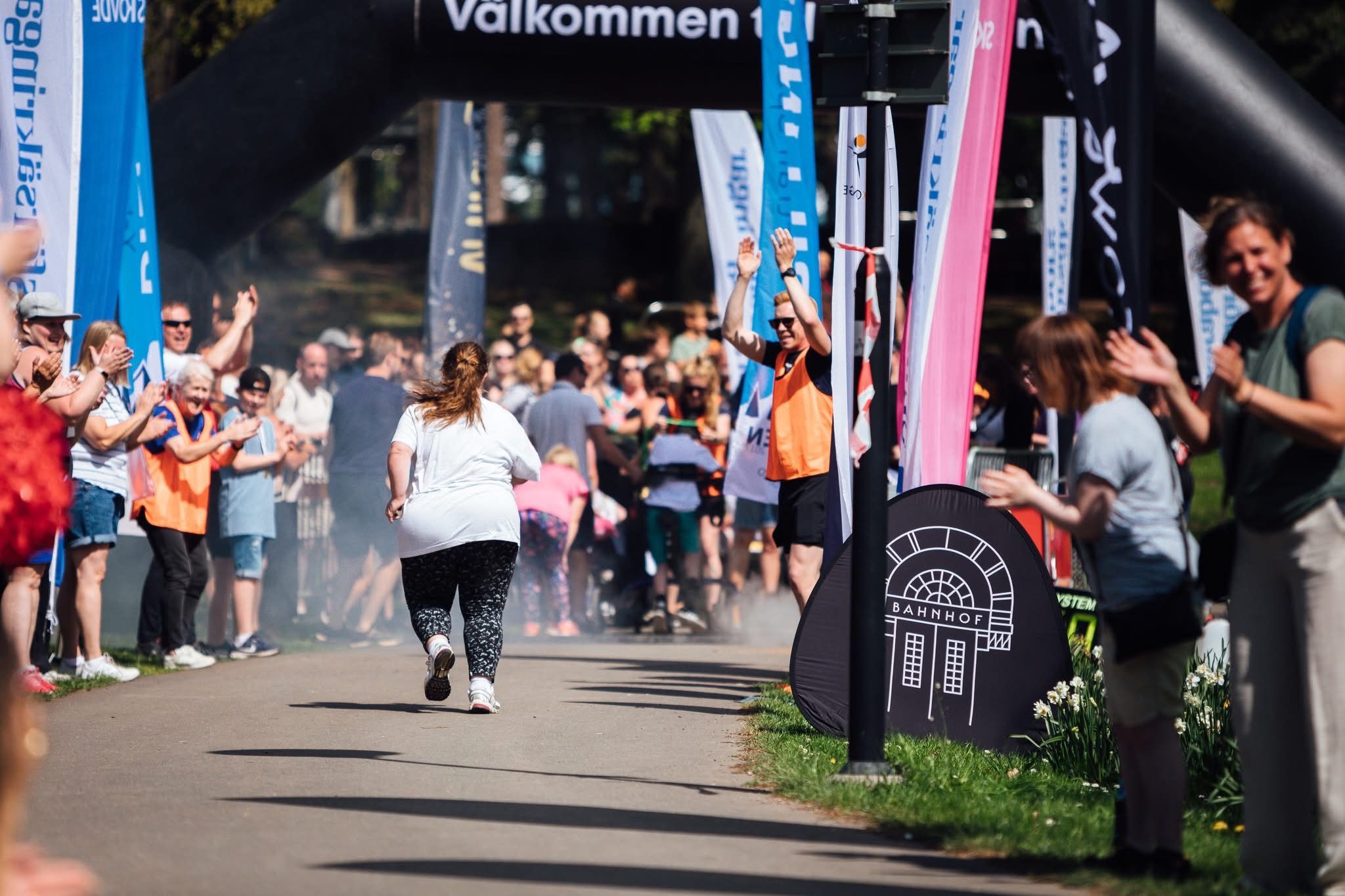 Girl running a race on an asphalt road. on both sides there is a crowed cheering her on.