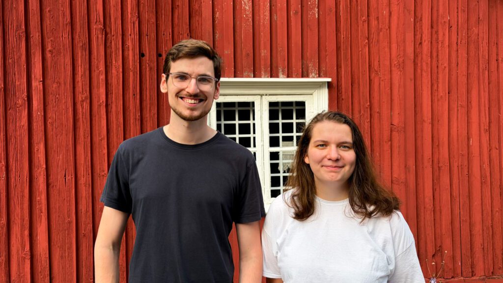 A man and a woman standing in front of a red wood wall.