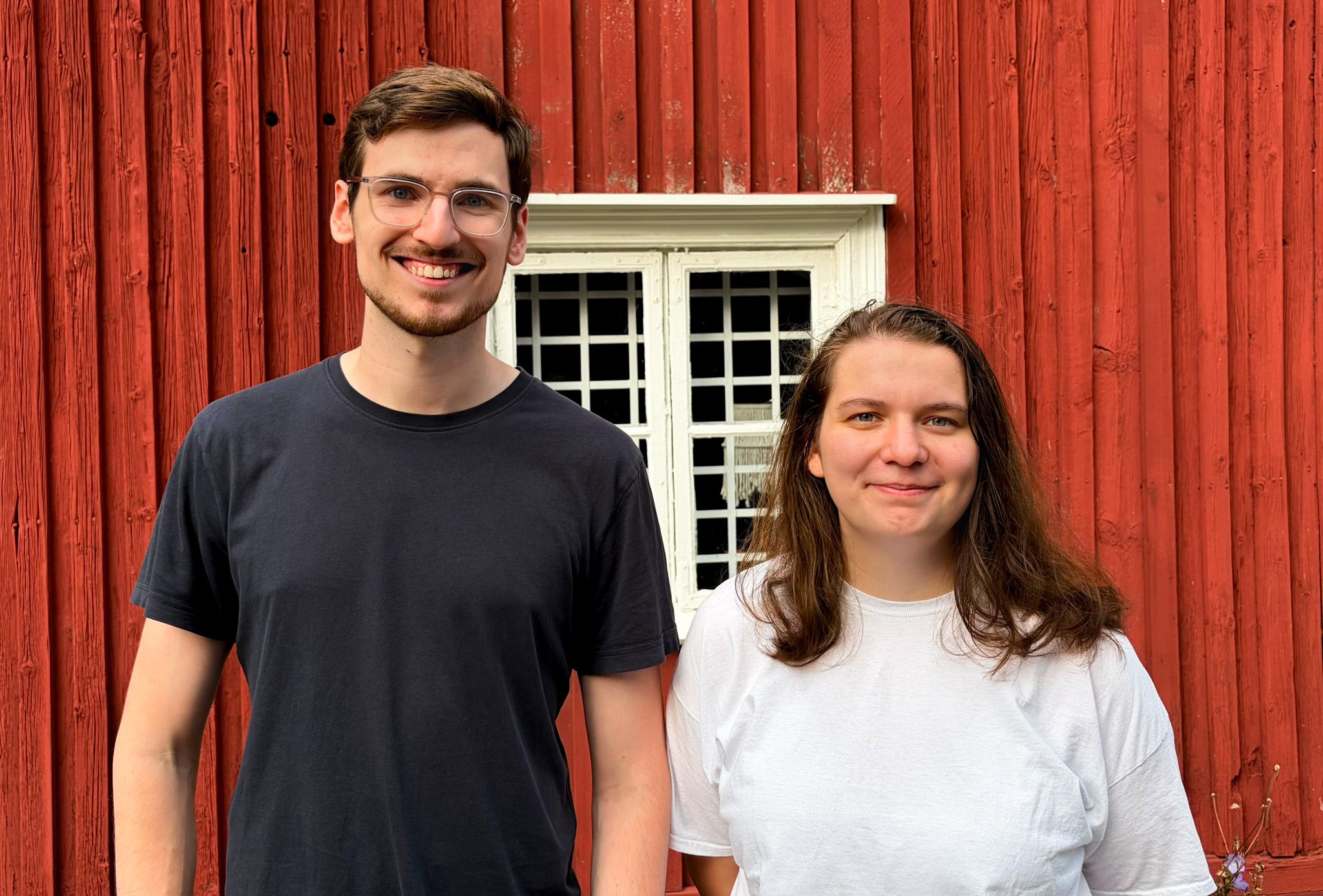 A man and a woman standing in front of a red wood wall.