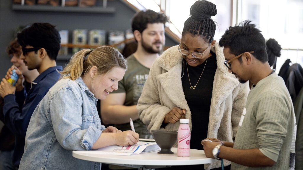 Three people are standing and talking at a table.