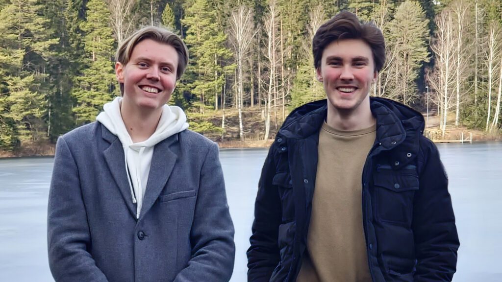 Två killar som står utomhus med en sjö och en skog i bakgrunden. Grundarna av Dazed Games i Skövde